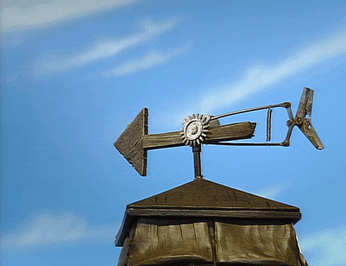 a weather vane on top of a roof with a blue sky in the background