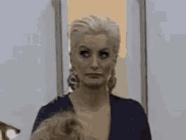a woman in a blue dress is standing in front of a door and making a funny face .