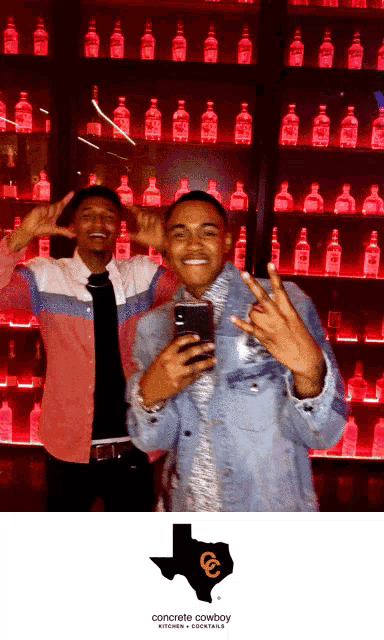 two men are posing for a picture in front of a concrete cowboy kitchen and cocktails wall