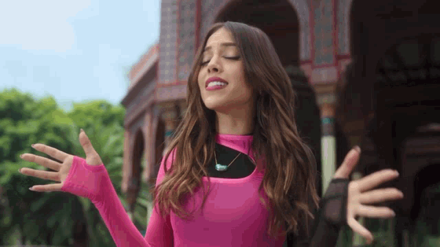 a woman in a pink top is standing with her arms outstretched in front of a building