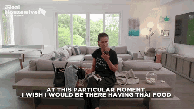 a woman is sitting on a couch looking at her phone with the words at this particular moment i wish i would be there