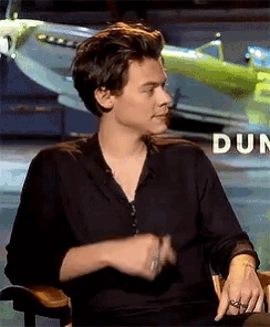 a man in a black shirt is sitting in front of a plane and making a funny face .