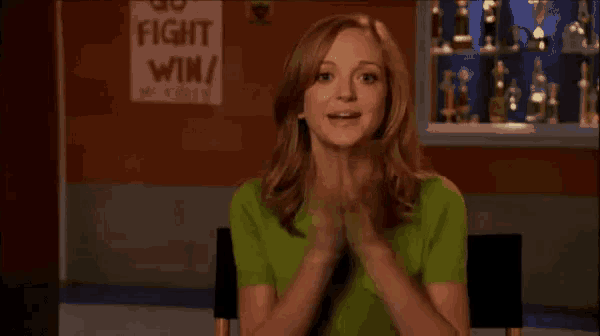 a woman in a green shirt is clapping in front of a sign that says go fight win