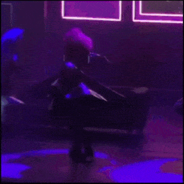 a person in a purple outfit is dancing in a dark room .