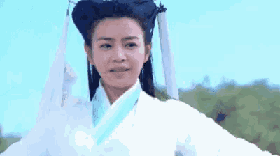 a woman in a white robe and a black hat is standing in a field .