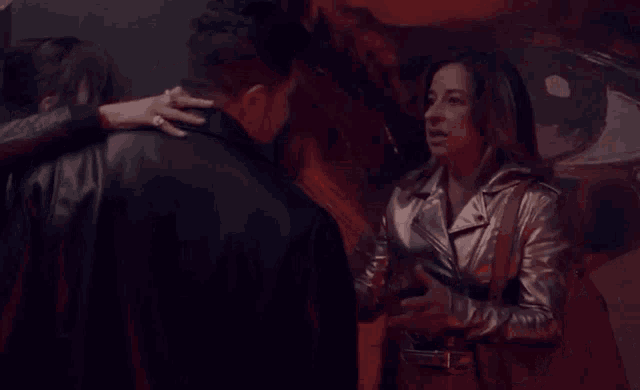 a woman in a silver leather jacket is hugging a man in a black jacket .