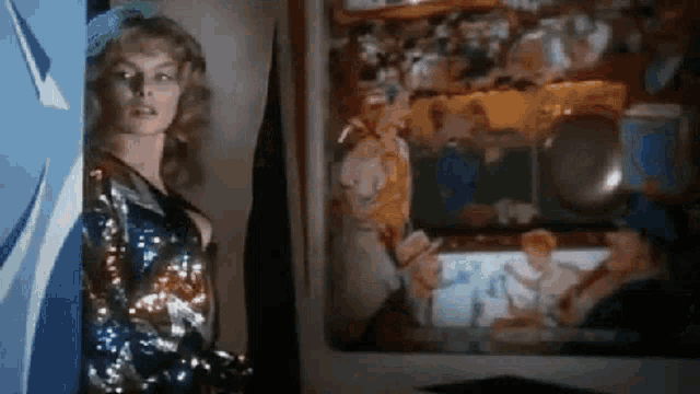 a woman in a sequined dress is standing in front of a mirror in a room .
