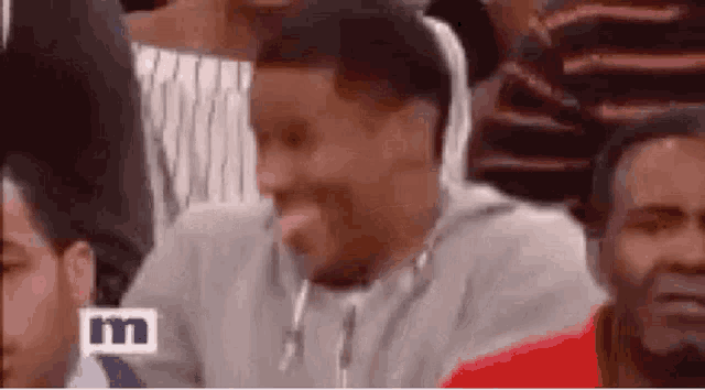 a man is sitting in a crowd of people laughing and making a funny face .