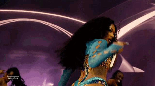 a woman in a blue and gold outfit is holding a microphone in front of a purple background that says coachella