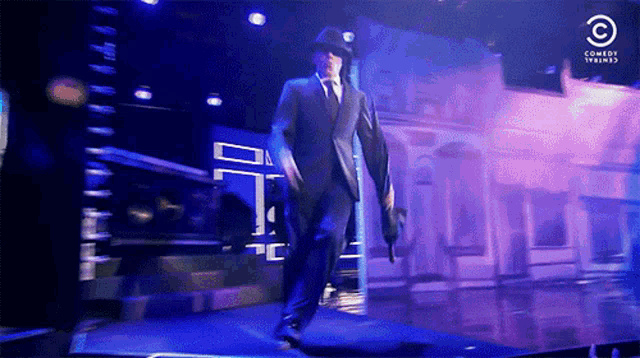 a man in a suit is walking on a stage with a comedy central logo in the corner