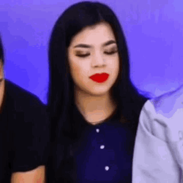 a woman with long black hair and red lipstick is sitting next to a man and a woman .