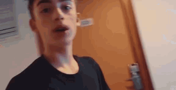 a young man in a black shirt is standing in front of a door in a hotel room .