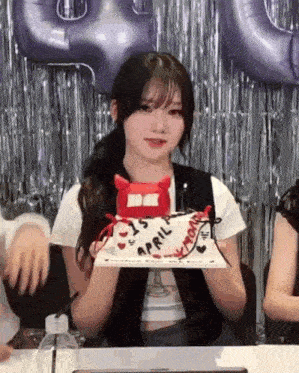 a girl is sitting at a table holding a birthday cake with a devil on it .