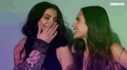 two women are laughing together and one is covering her mouth .