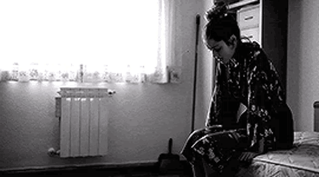 a black and white photo of a woman sitting on a bed in a room .