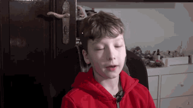 a young boy wearing a red hoodie is sitting in a chair