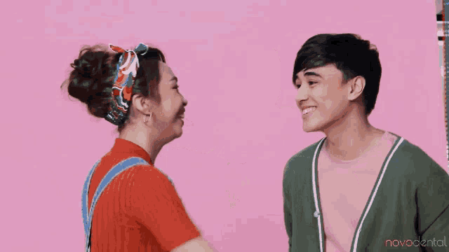 a woman is hugging a man on a pink background with novodental written on the bottom