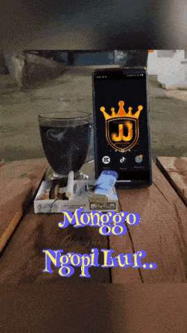 a phone with a crown on it sits on a table next to a cup of coffee and a pack of cigarettes