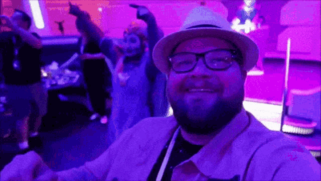 a man wearing glasses and a hat is smiling in front of a purple background