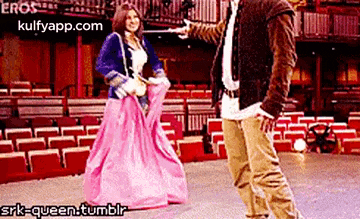 a man and a woman are standing next to each other in front of an auditorium . the woman is wearing a pink dress .