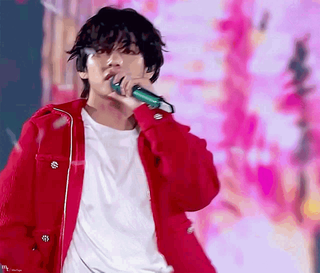 a man in a red jacket is singing into a microphone while wearing a white shirt .