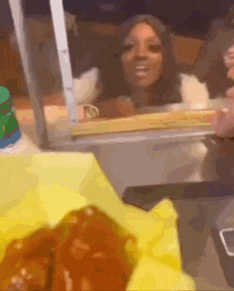 a blurry picture of a woman looking out a window at a table with food and a cell phone .