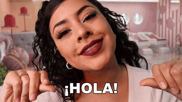 a woman is smiling and pointing at herself with the words " hola " written on her chest