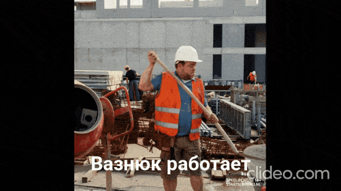 a man wearing an orange vest and a white hard hat is standing in front of a concrete mixer on a construction site