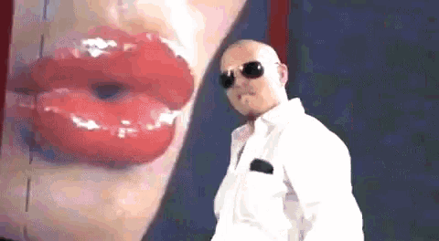 a bald man wearing sunglasses stands in front of a large red lip