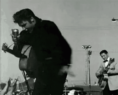 a black and white photo of elvis presley playing a guitar and singing into a microphone on stage .