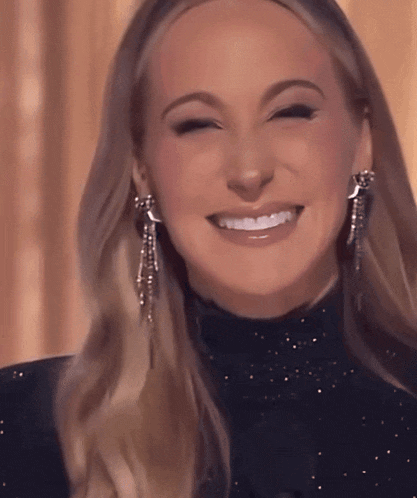 a woman wearing a black turtleneck and silver earrings smiles with her eyes closed