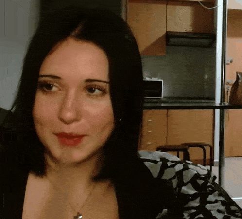 a woman wearing a black shirt and a necklace looks at the camera