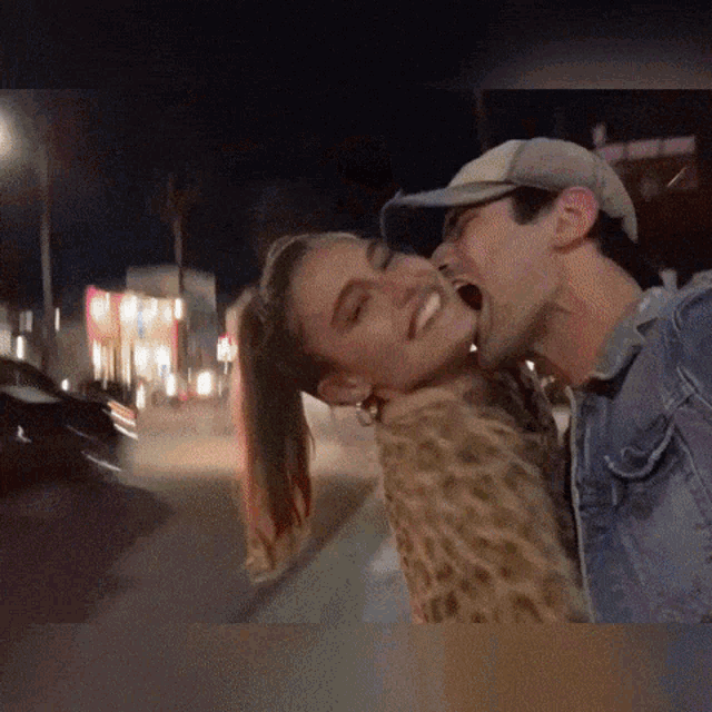 a man is kissing a woman on the cheek while wearing a baseball cap