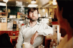 a man with a beard is sitting at a table in a restaurant talking to another man