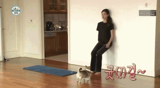 a woman is leaning against a wall with a dog standing next to her .