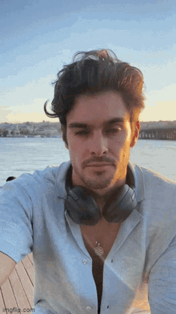 a man wearing headphones takes a selfie in front of the ocean