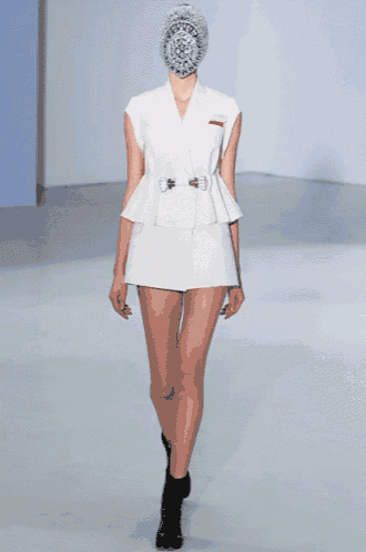 a model walks down a runway wearing a white dress and a hat