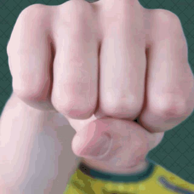 a close up of a person 's fist with a yellow shirt behind it