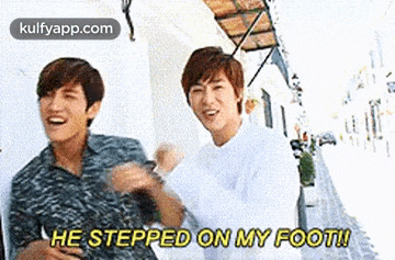 two young men are standing next to each other on a sidewalk and one of them is saying `` he stepped on my foot ! ''