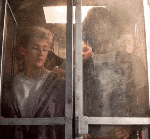 a man in a purple shirt looks out of a window
