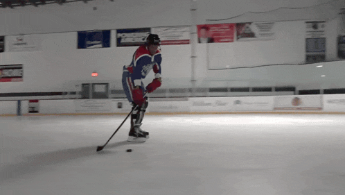a hockey player in a red white and blue uniform stands on the ice holding a puck