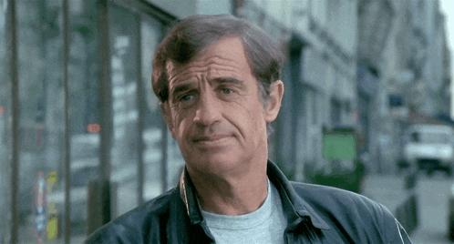 a man with a gray shirt and a black jacket is standing on a street