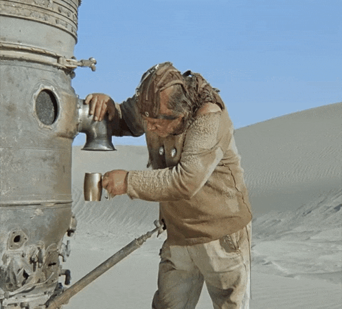 a man wearing a helmet holds a cup in his hand while standing in the desert