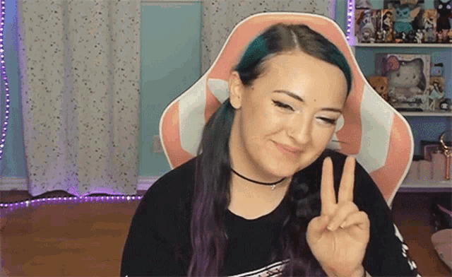 a woman with purple hair is sitting in a pink and white chair making a peace sign