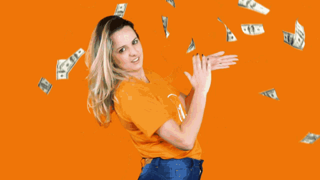a woman in an orange shirt with the letter u on it stands in front of a pile of money