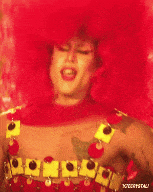 a drag queen with red hair is wearing a red and yellow outfit with xtecrystali written below her