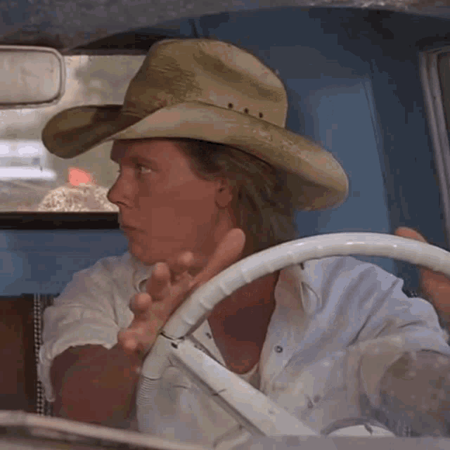 a man wearing a cowboy hat and white shirt is driving a car
