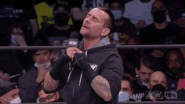 a wrestler is holding a microphone in front of a crowd while wearing a mask .