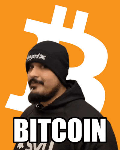 a man with a beard wearing a black beanie and a black hoodie stands in front of a bitcoin sign