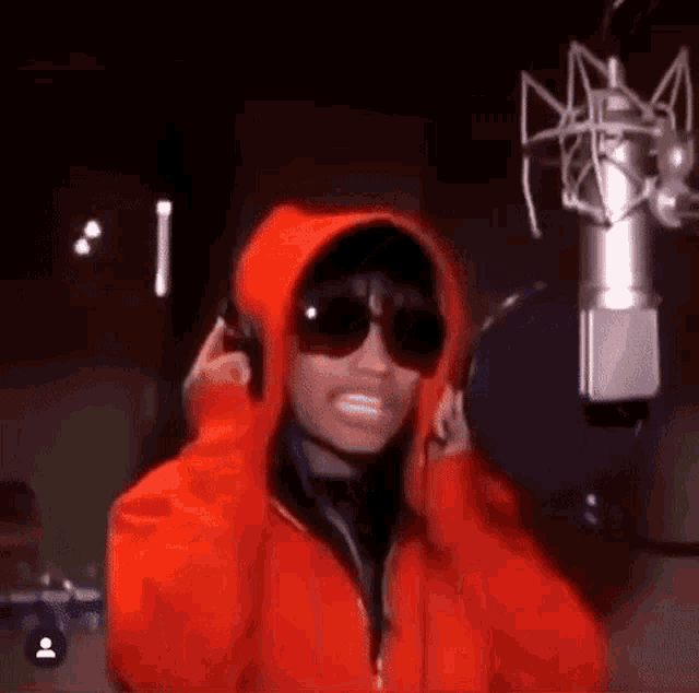 a woman wearing sunglasses and a red hoodie is standing in front of a microphone .